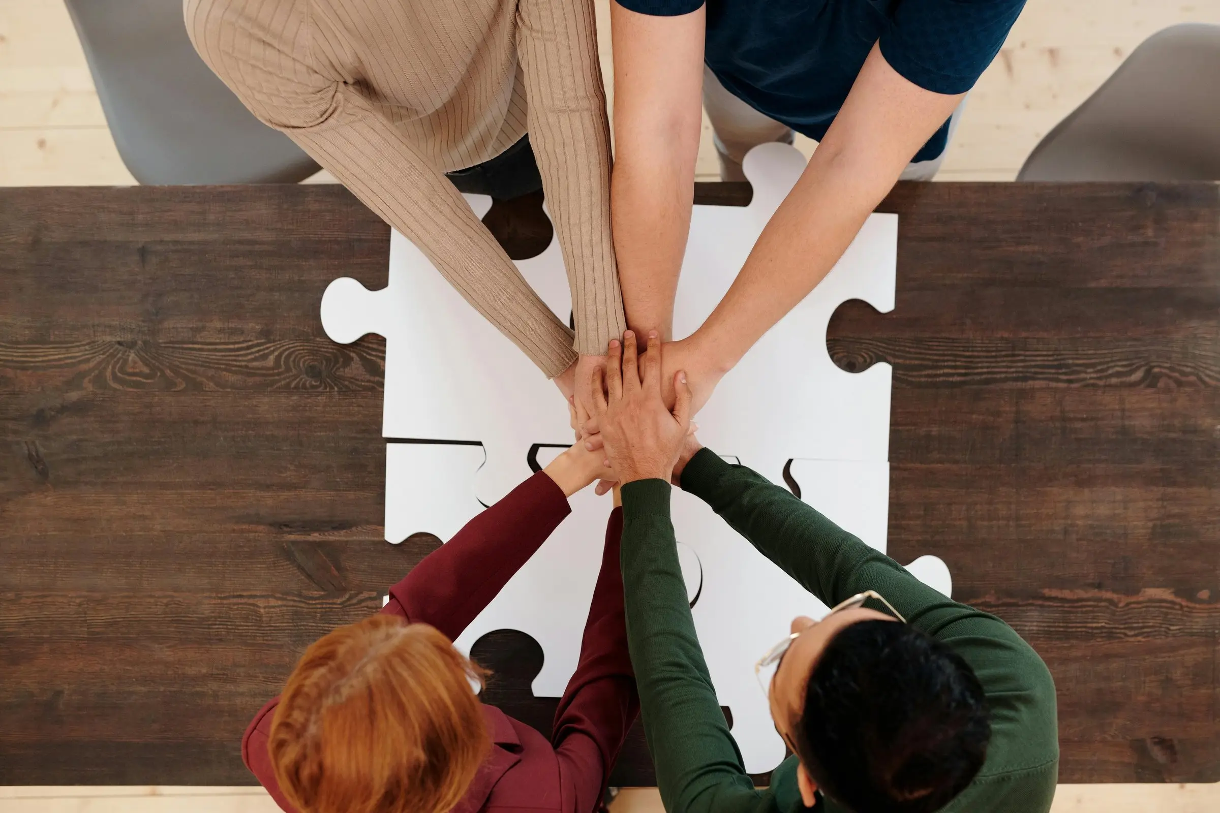 People placing hands together over a jigsaw puzzle on a wooden table